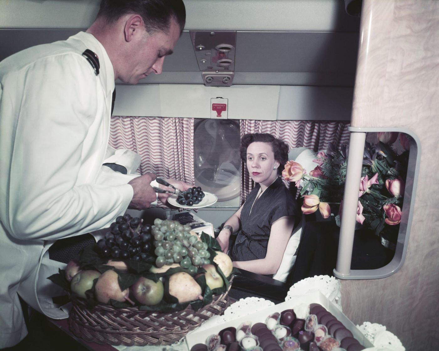 An air steward serves a plate of grapes to a female passenger from a basket of fruit on a Bristol Britannia medium to long range airliner in October 1956.