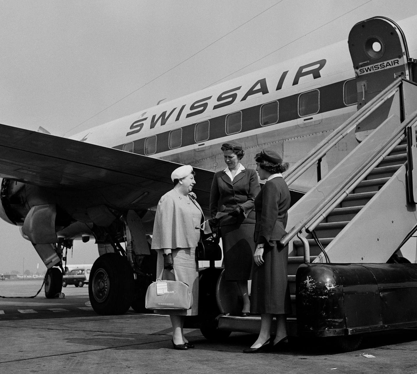 Two air hostesses welcome a passenger boarding a Swiss Air aircraft at London Airport in the 1950s.
