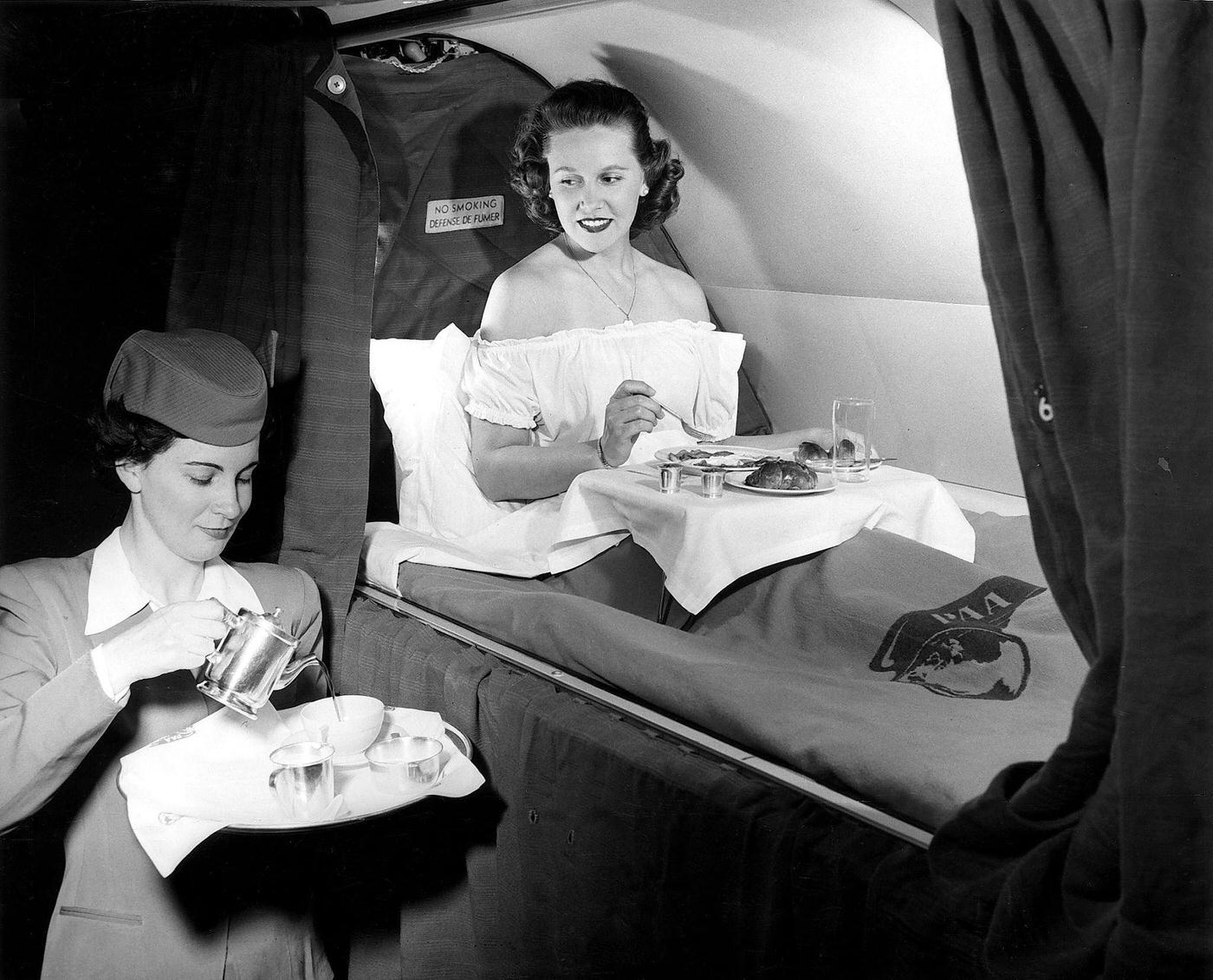 A PAA Atlantic Division stewardess serves breakfast in bed to a female passenger during a transatlantic flight in 1952.