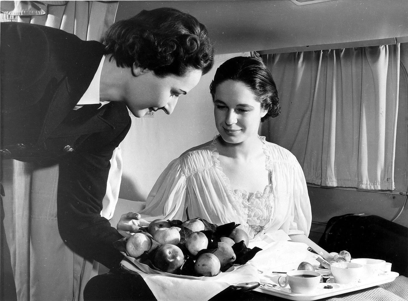 A BOAC airline stewardess serves breakfast in bed to a passenger on a BOAC Speedbird Stratocruiser in 1952.