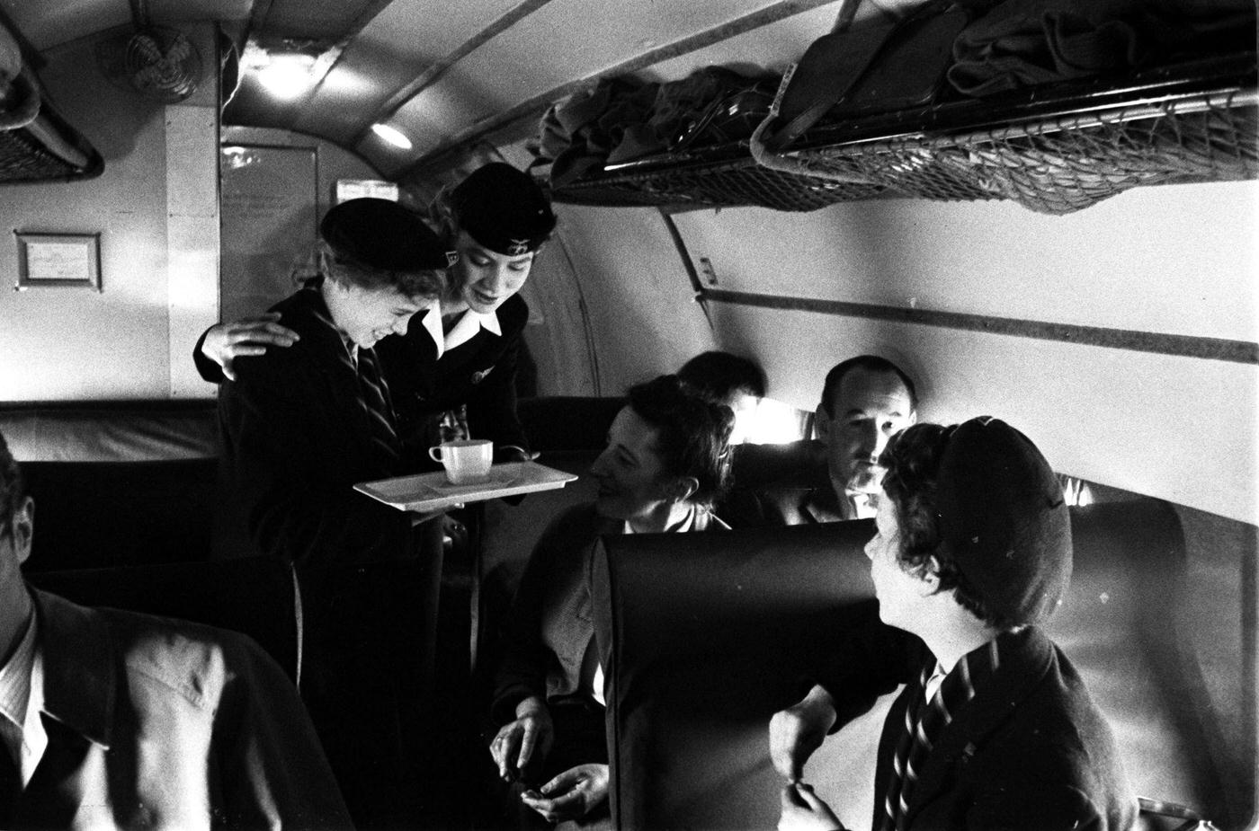 Air hostesses are captured serving passengers on a plane in 1955.