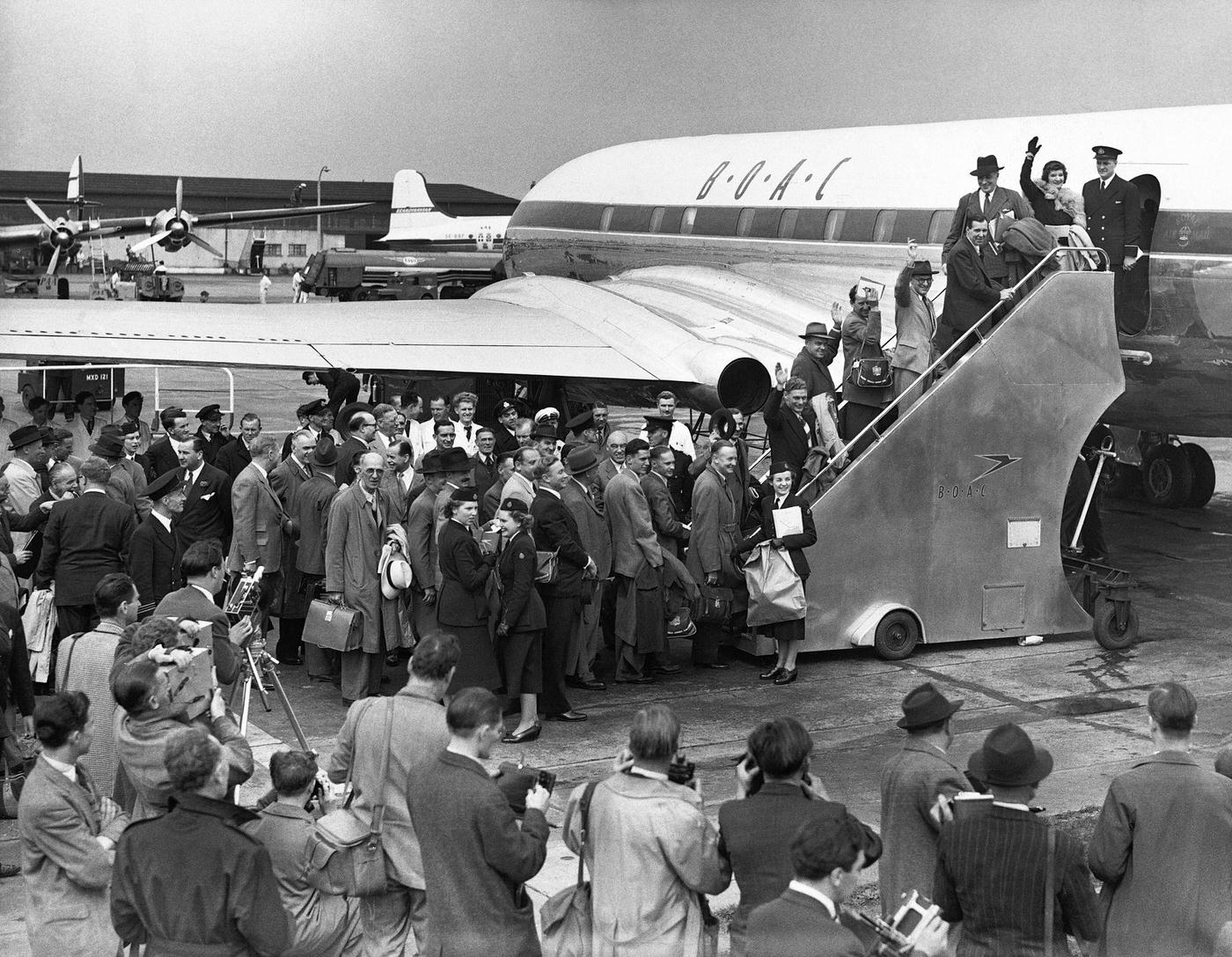 The first passengers of the world's inaugural jet service board their plane bound for Johannesburg, while nearby reporters capture the event.