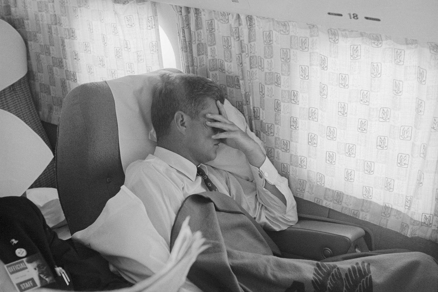 John F. Kennedy resting in the passenger cabin of an airplane during his 1960 campaign.