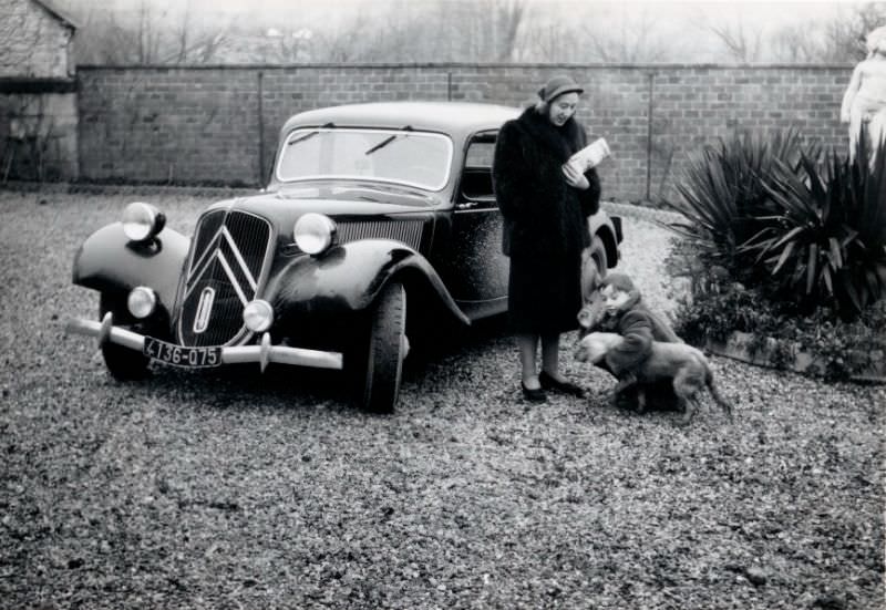 Lady, boy, and dog with Citroën 11 CV in graveled yard in wintertime, Paris registration, 1955