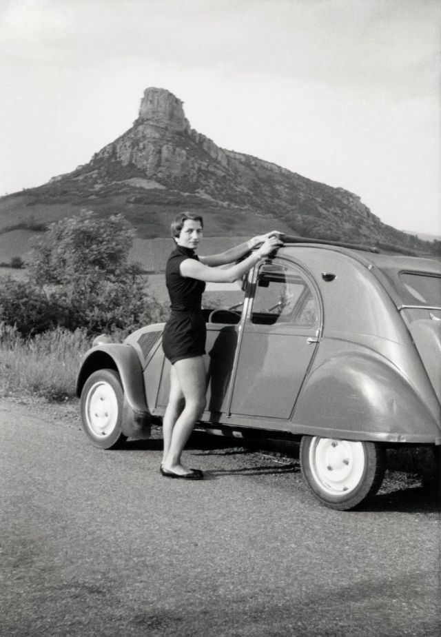 Lady with Citroën 2 CV in countryside with vineyards and Roche de Solutré in the distance, June 1, 1955