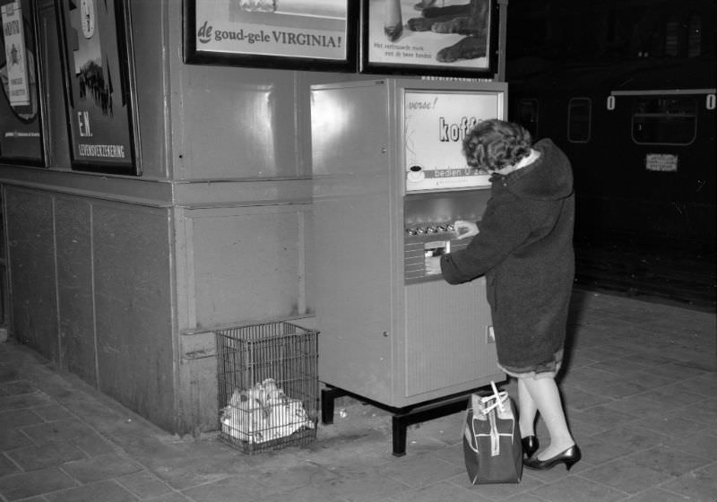Lady gets coffee from a vending machine at Amsterdam Central Station. The device is placed against the back of the freight elevator, October 19, 1959