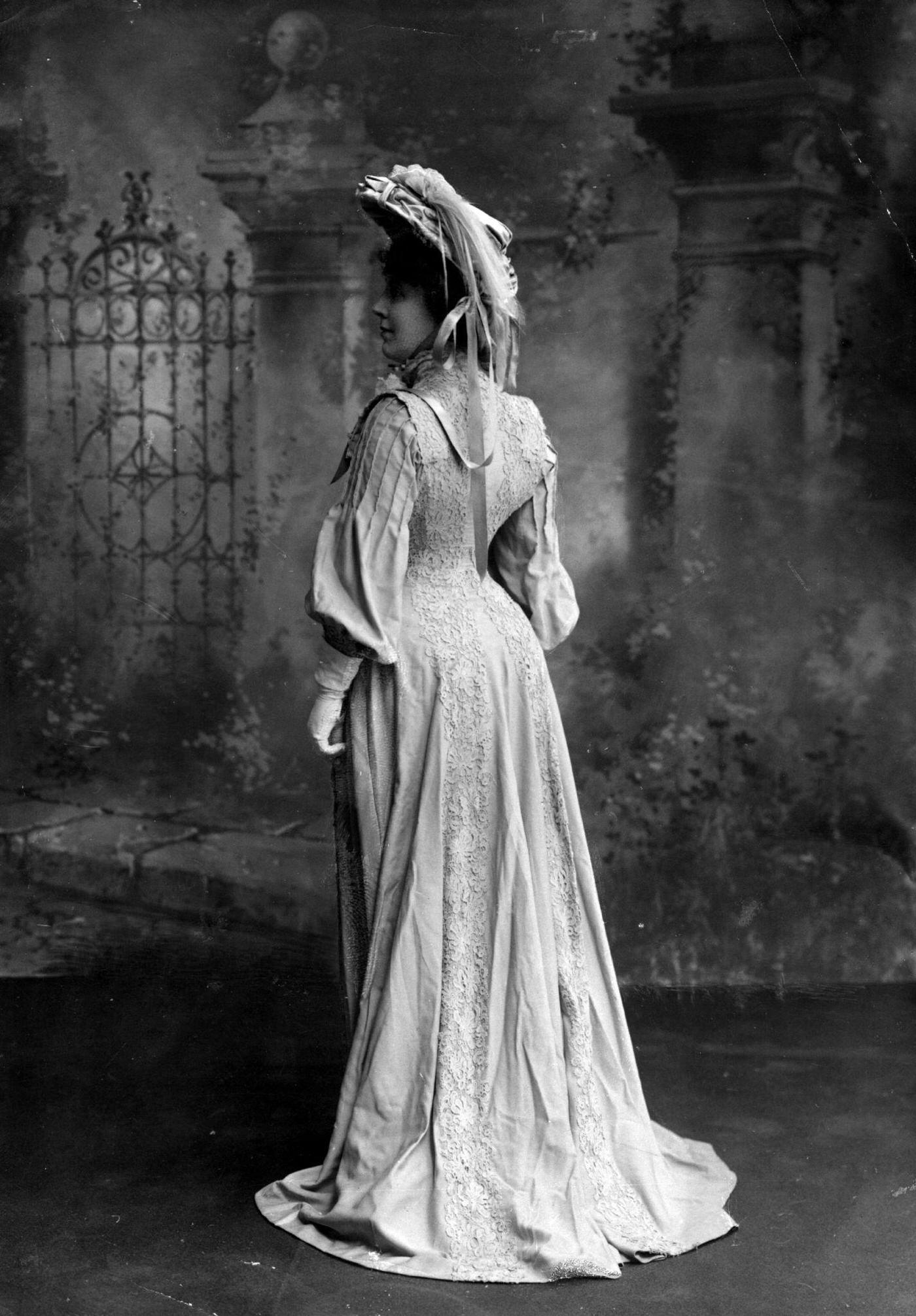 Miss Mansfield wears a coatdress with lace detail and full sleeves, complete with a feather-trimmed hat