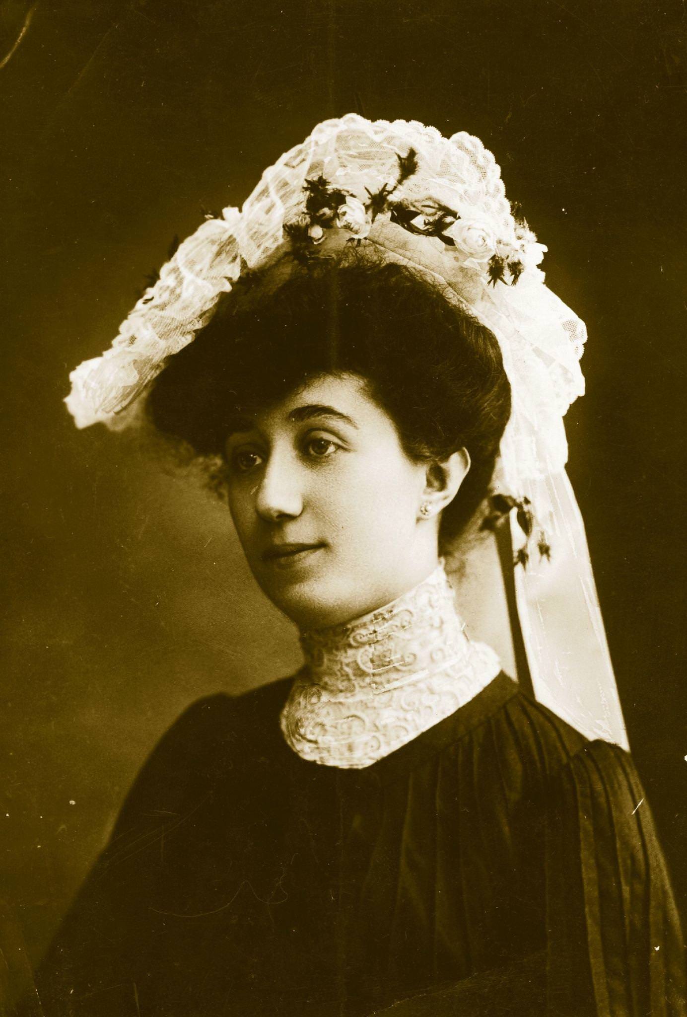 An Edwardian lady wears a high-necked blouse and hat with lace and flower trimmings