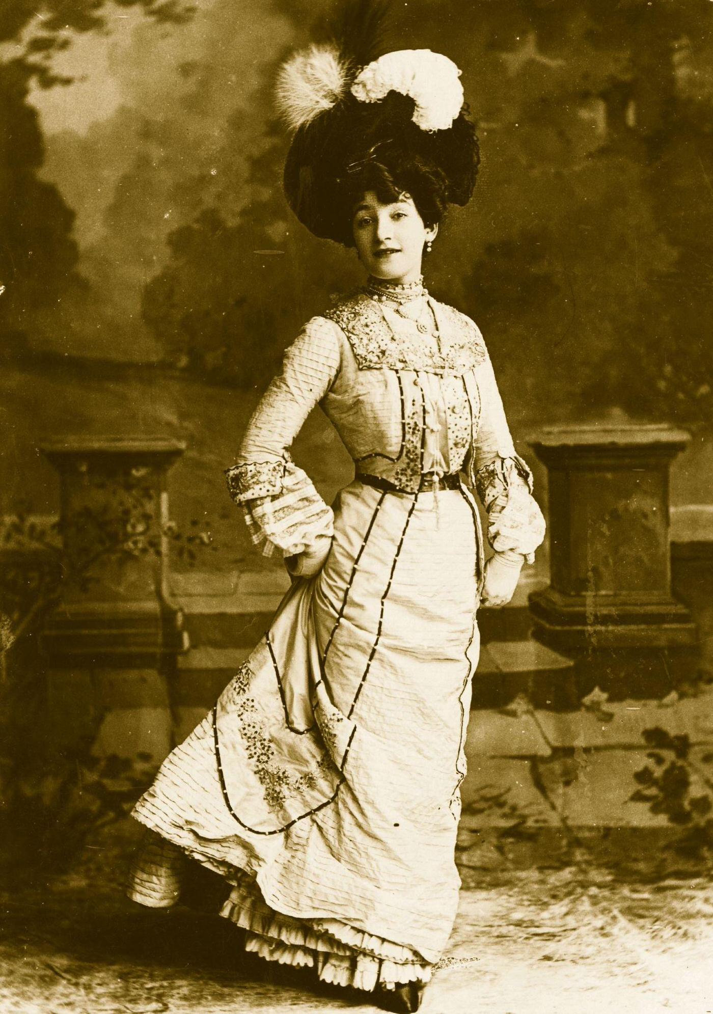 An Edwardian lady wears a high-necked blouse and hat with lace and flower trimmings