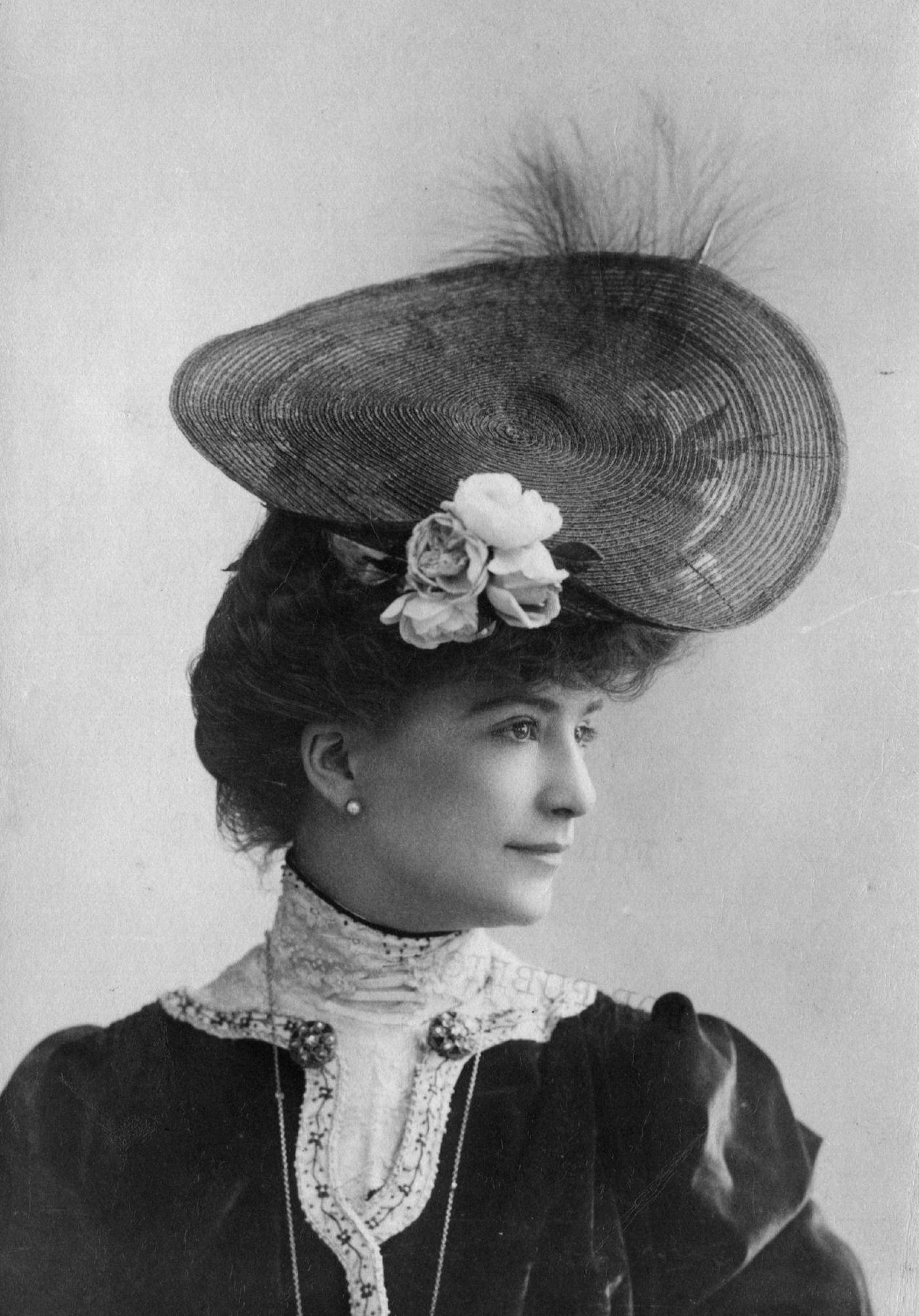 An Edwardian woman wears a circular hat with flower and feather trimming in 1903