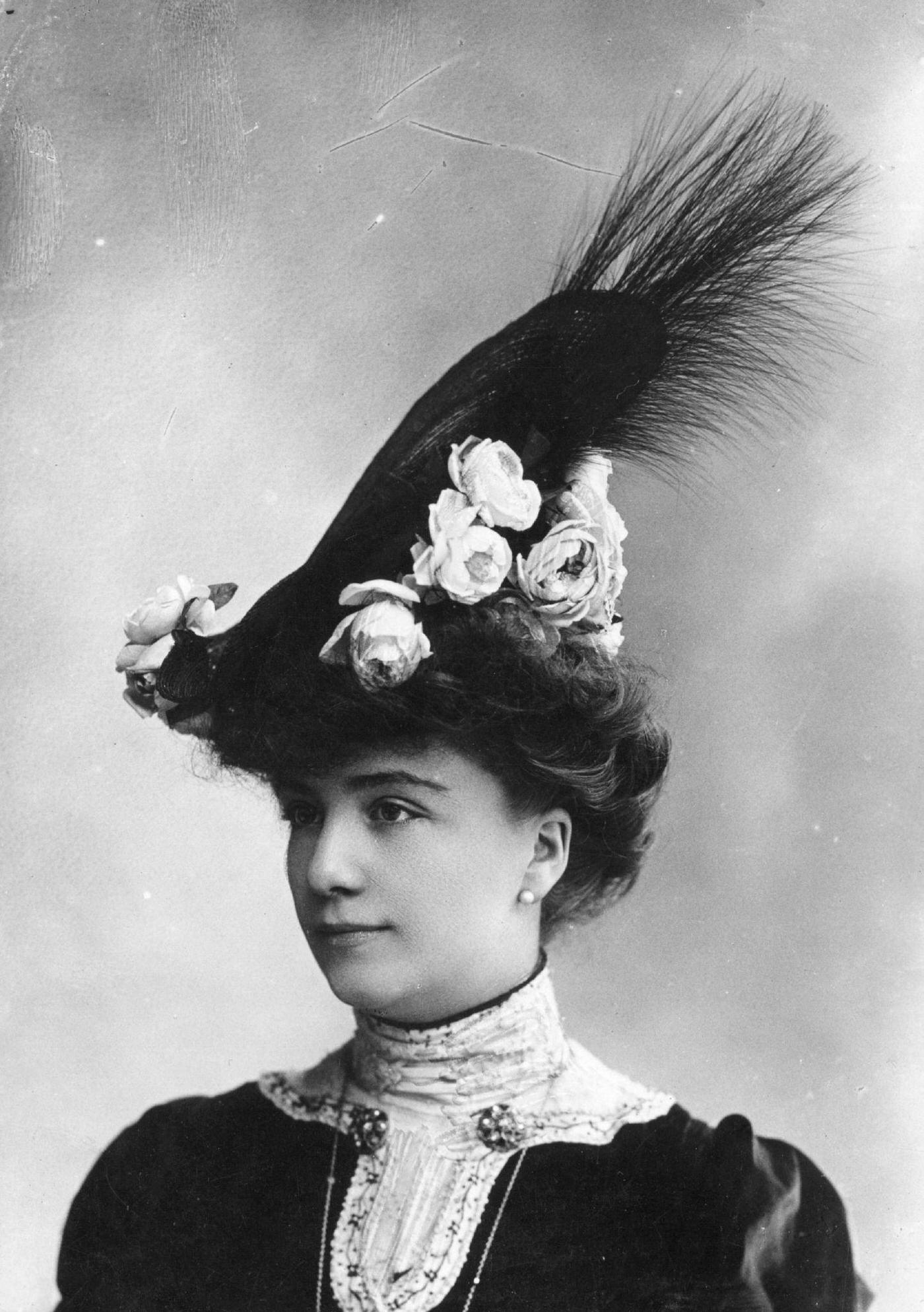 An Edwardian woman wears a high hat decorated with flowers and feathers in 1903