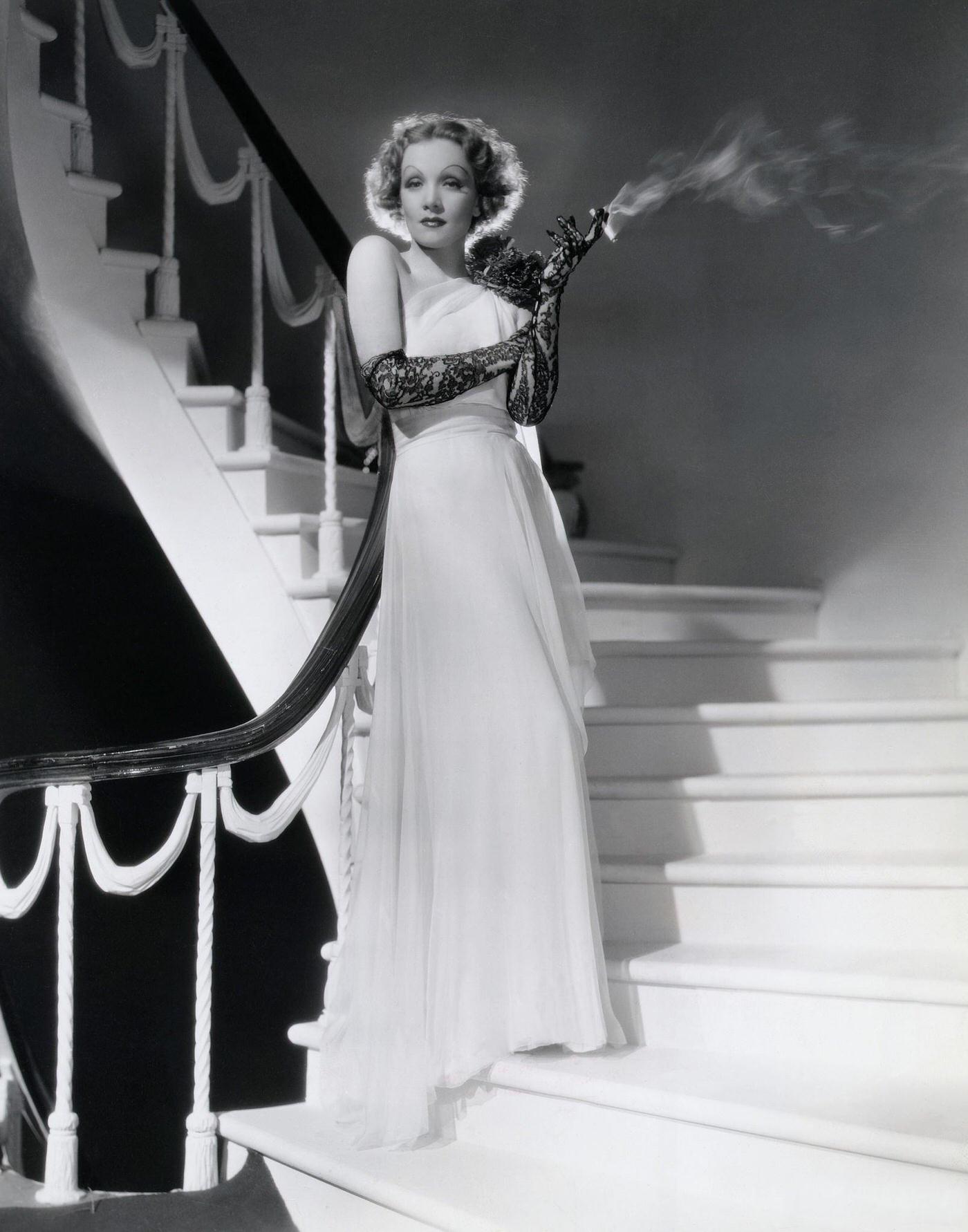 Marlene Dietrich is captured smoking on a staircase.