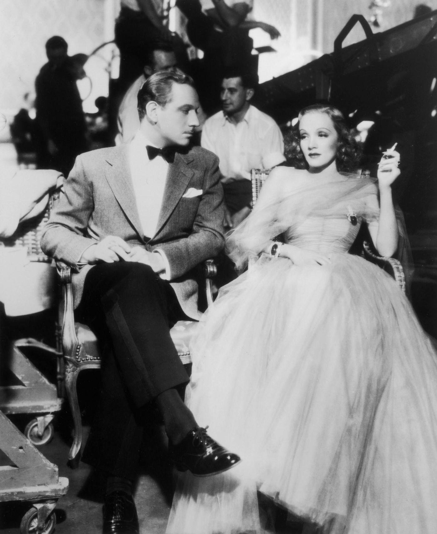Melvyn Douglas sits next to German-born actress Marlene Dietrich as she smokes a cigarette in 1937.