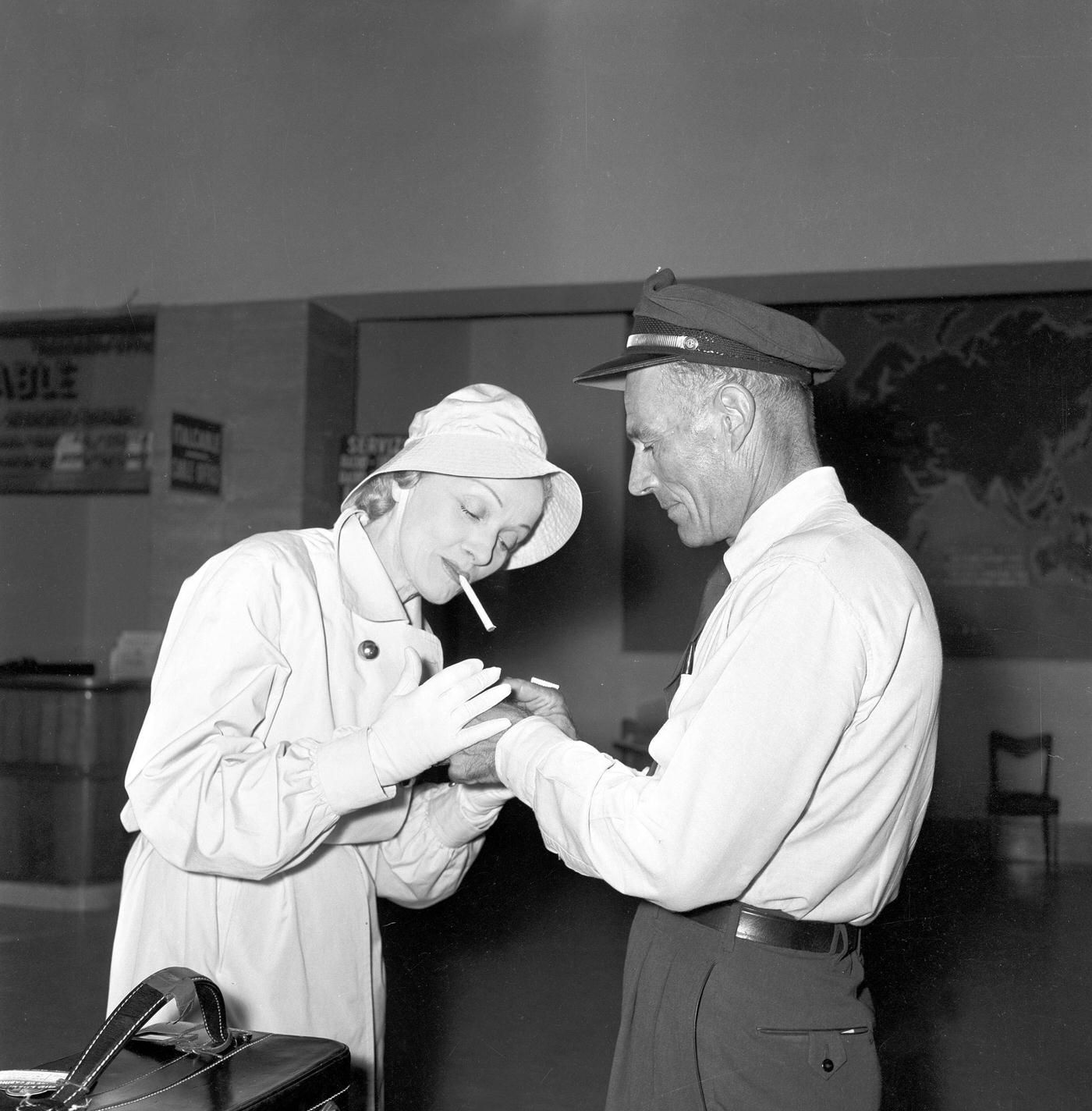 Marlene Dietrich asks a security worker to light her cigarette.