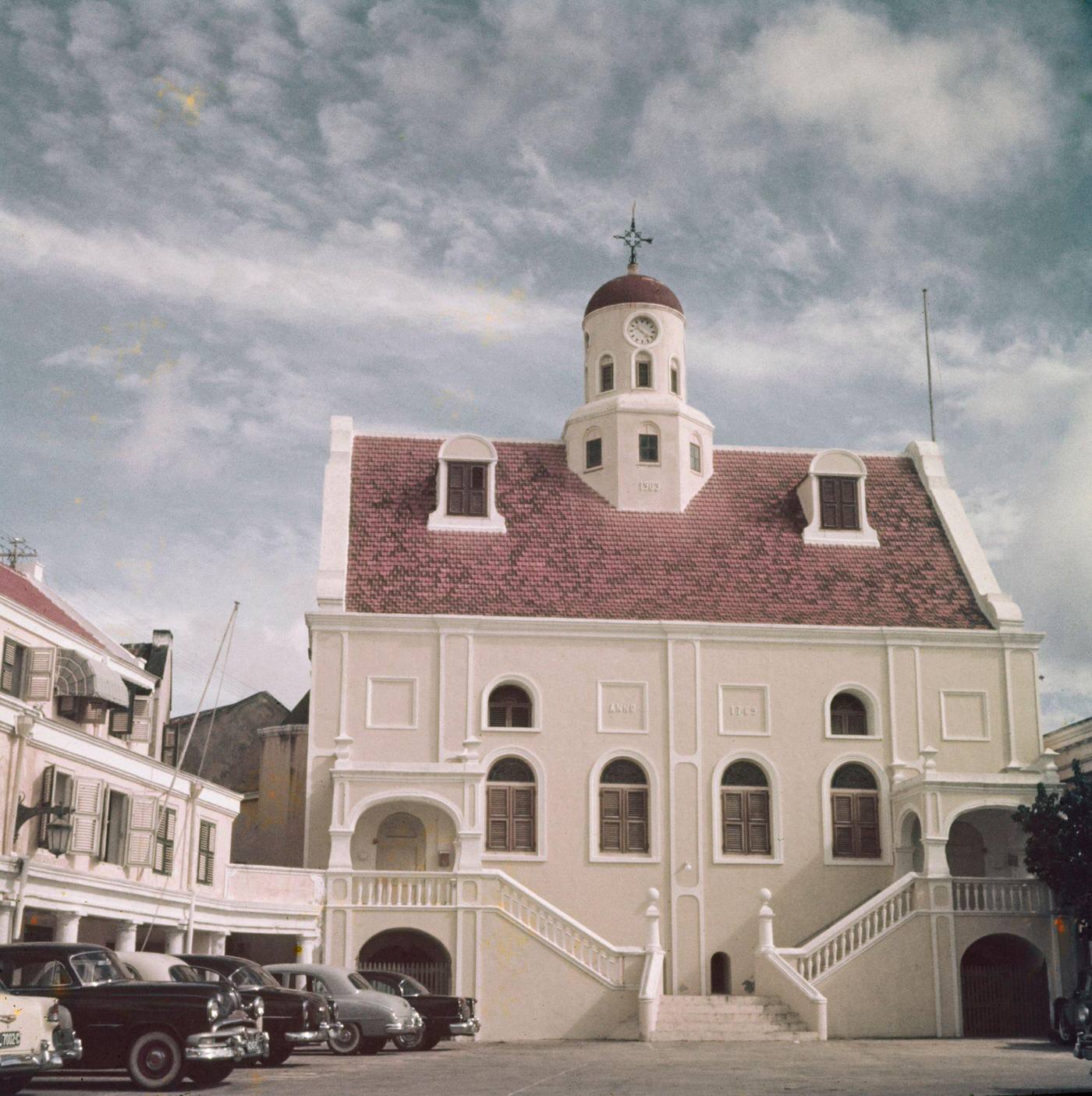 Cars parked outside a Dutch colonial building in Willemstad, capital city of the island of Curaçao, part of the Kingdom of the Netherlands in the southern Caribbean Sea, 1955.