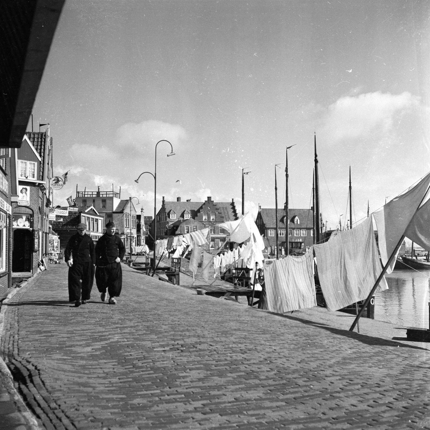 Two men in traditional baggy trousers walking through Volendam harbour in the western Netherlands, 1955.