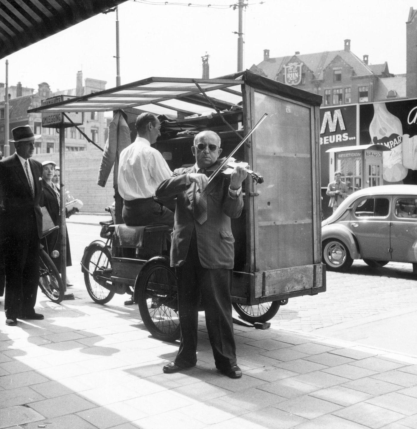 Two musicians, one playing an organ and the other a violin, performing in a street in the Netherlands, 1955.