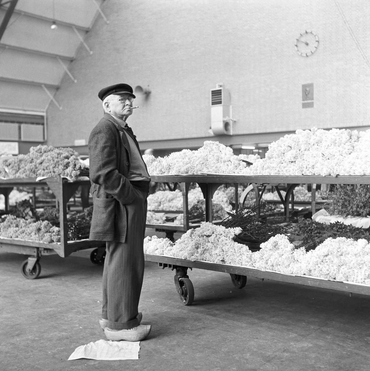 A man wearing traditional Dutch clogs with flower carts in the background, Amsterdam, the Netherlands, 1954.