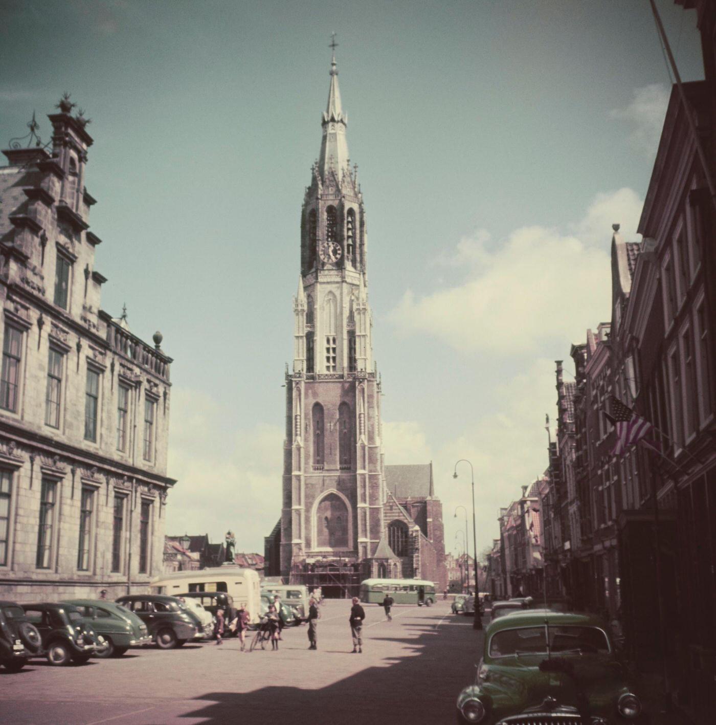 Pedestrians pass cars parked beside City Hall on Markt Square in front of Nieuwe Kerk Protestant church in the center of the city of Delft in the province of South Holland in the Netherlands 1950.