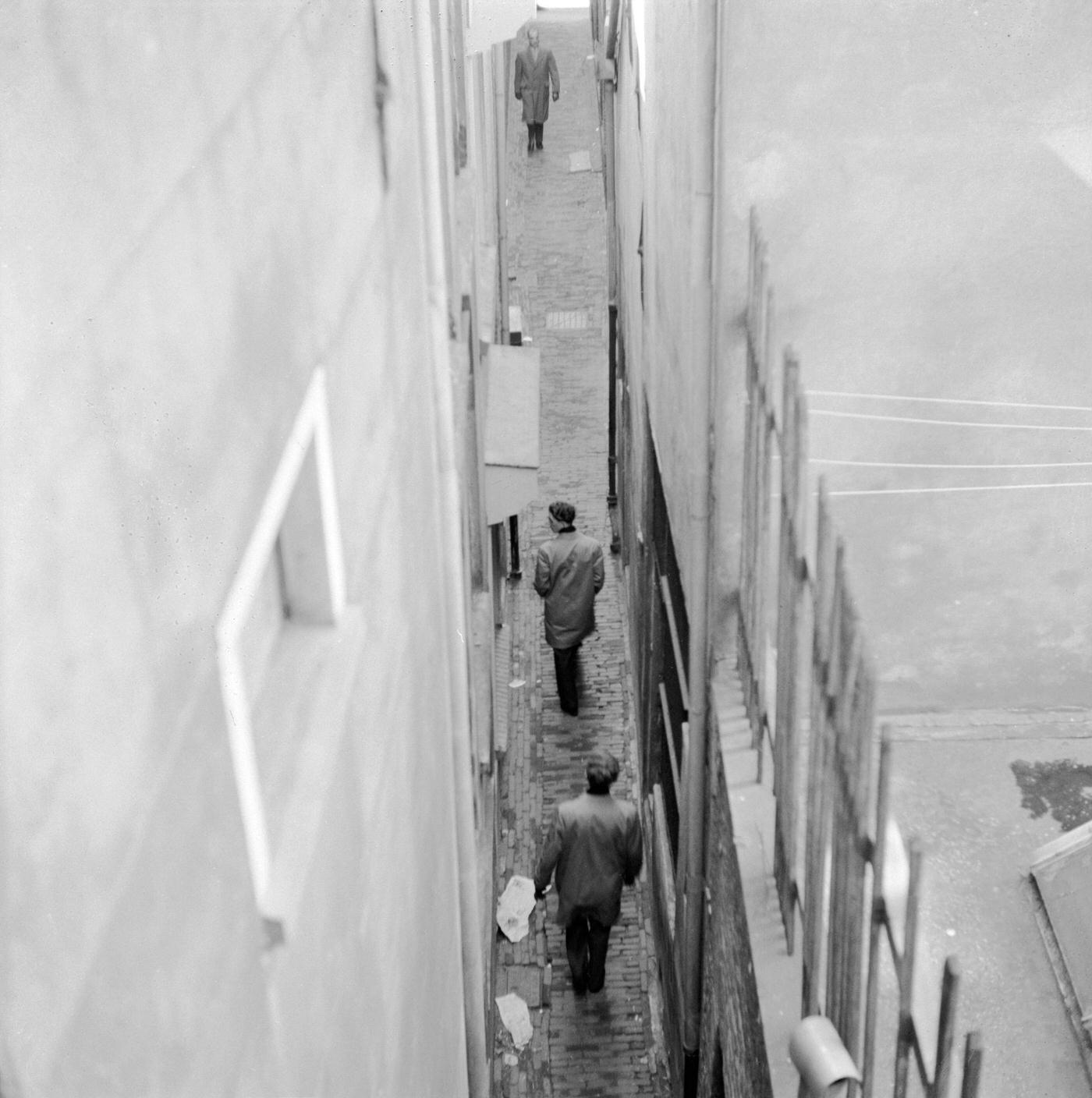 Men walking down a narrow alley in the Netherlands, circa 1956.