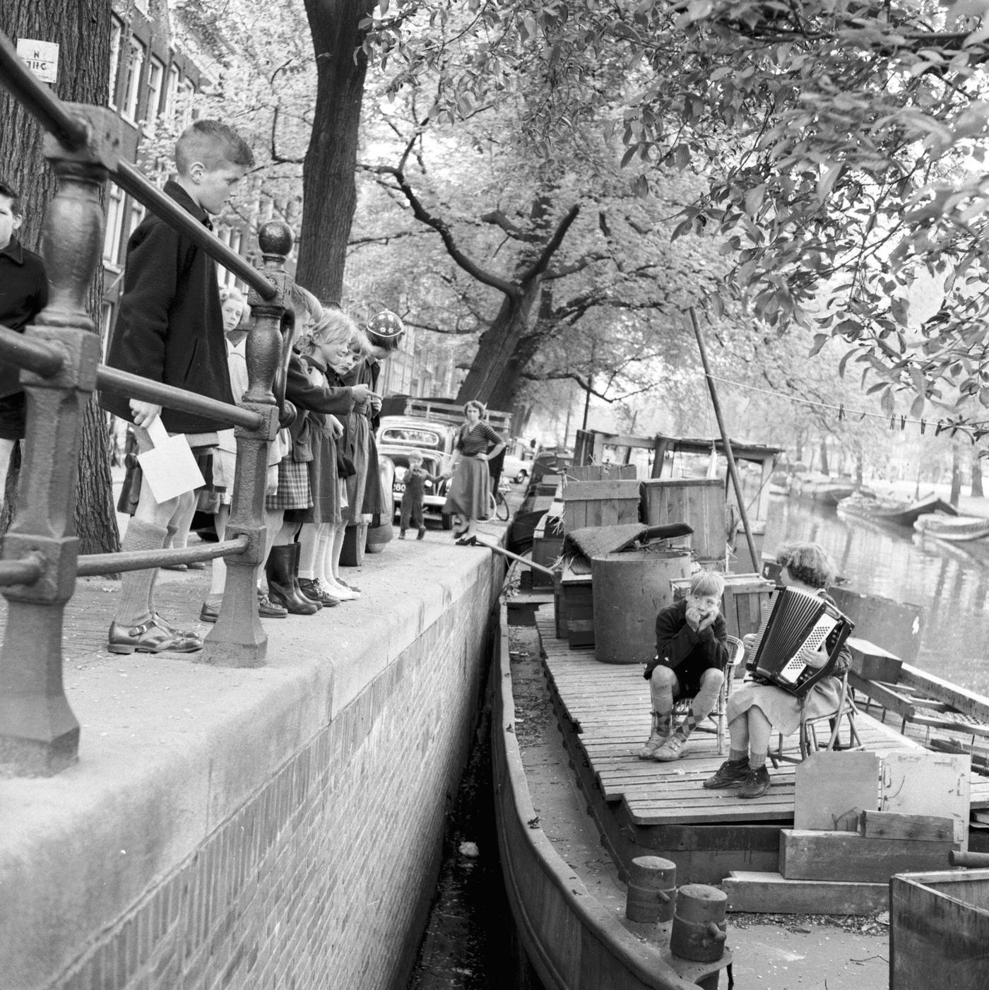 Sjoerttje van der Geest plays an accordion for the benefit of everybody along the canal from the deck of her parent's houseboat 'Diepwijk' in Amstel, Amsterdam, 12th November 1955.