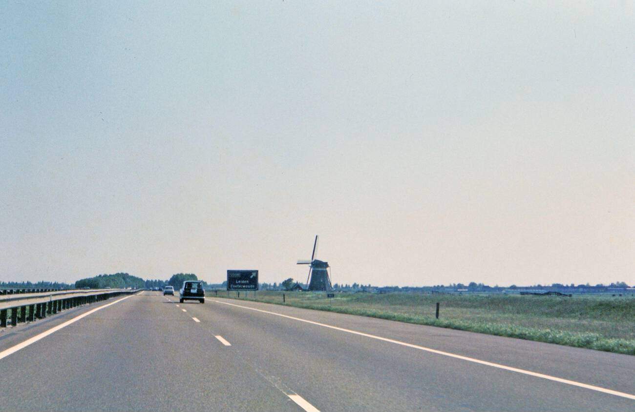 A car driving on a highway near Leiden, The Netherlands, with a windmill visible on the side of the highway, in 1972.