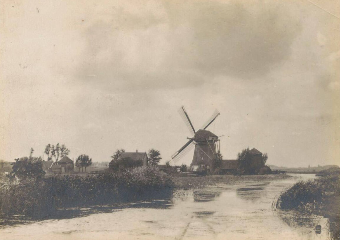 View of a windmill and farms on a river, Netherlands, 1900