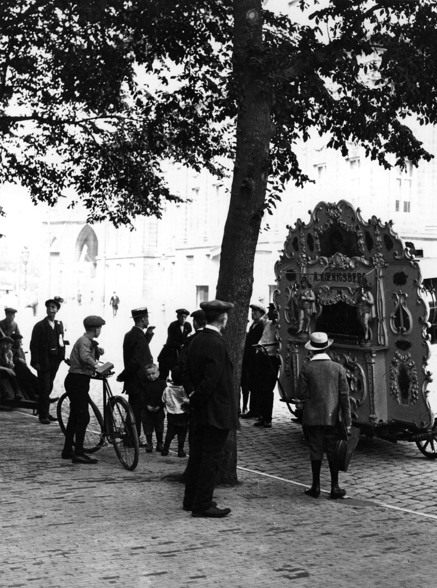 Passers-by stop to listen to a barrel organ, in a town in Holland, 1900