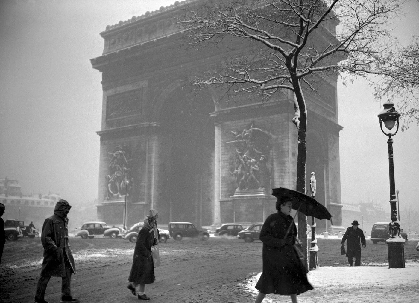 People Walking In The Muddy Snow Near The Arc de Triomphe, Paris, During The 1952 Winter.