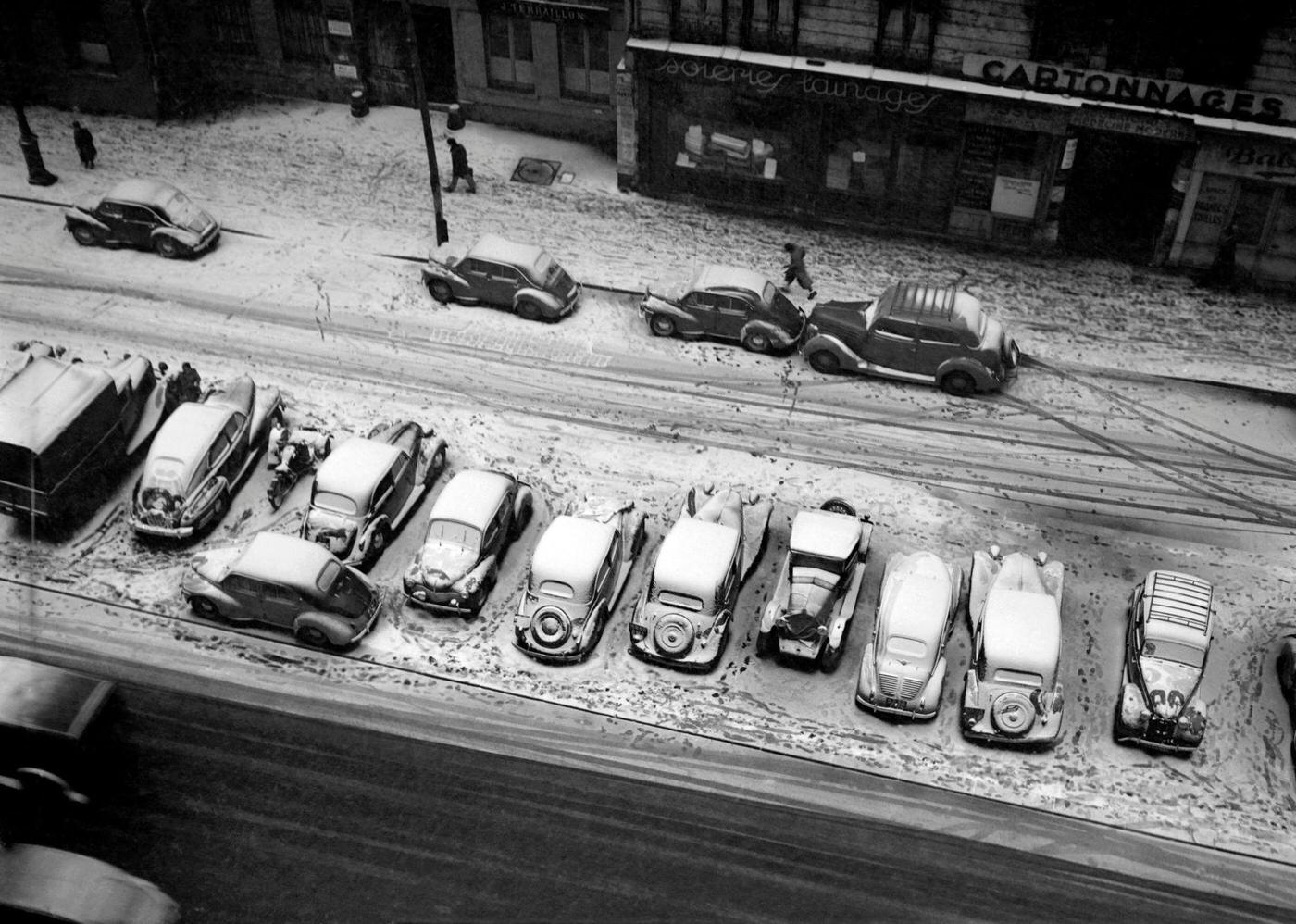 A Man Walking By Cars Covered In Snow In A Street Of Paris, In The 1950s.