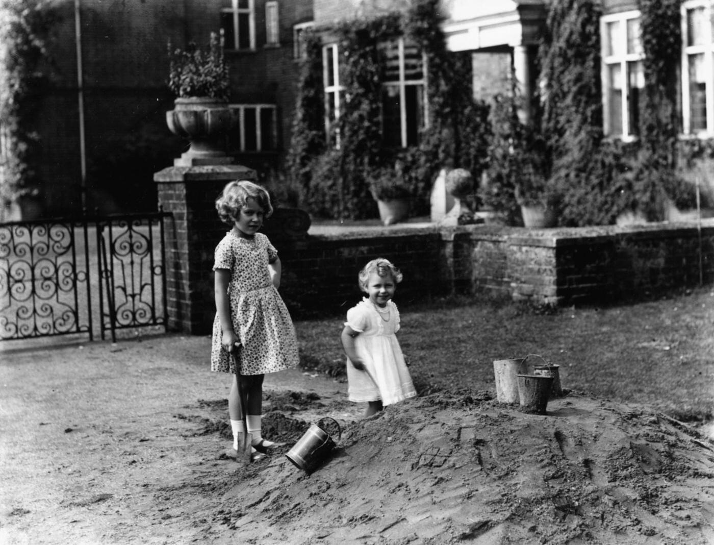 Princess Elizabeth (left) and Princess Margaret playing together outdoors beside a pile of sand, August 12th 1932.
