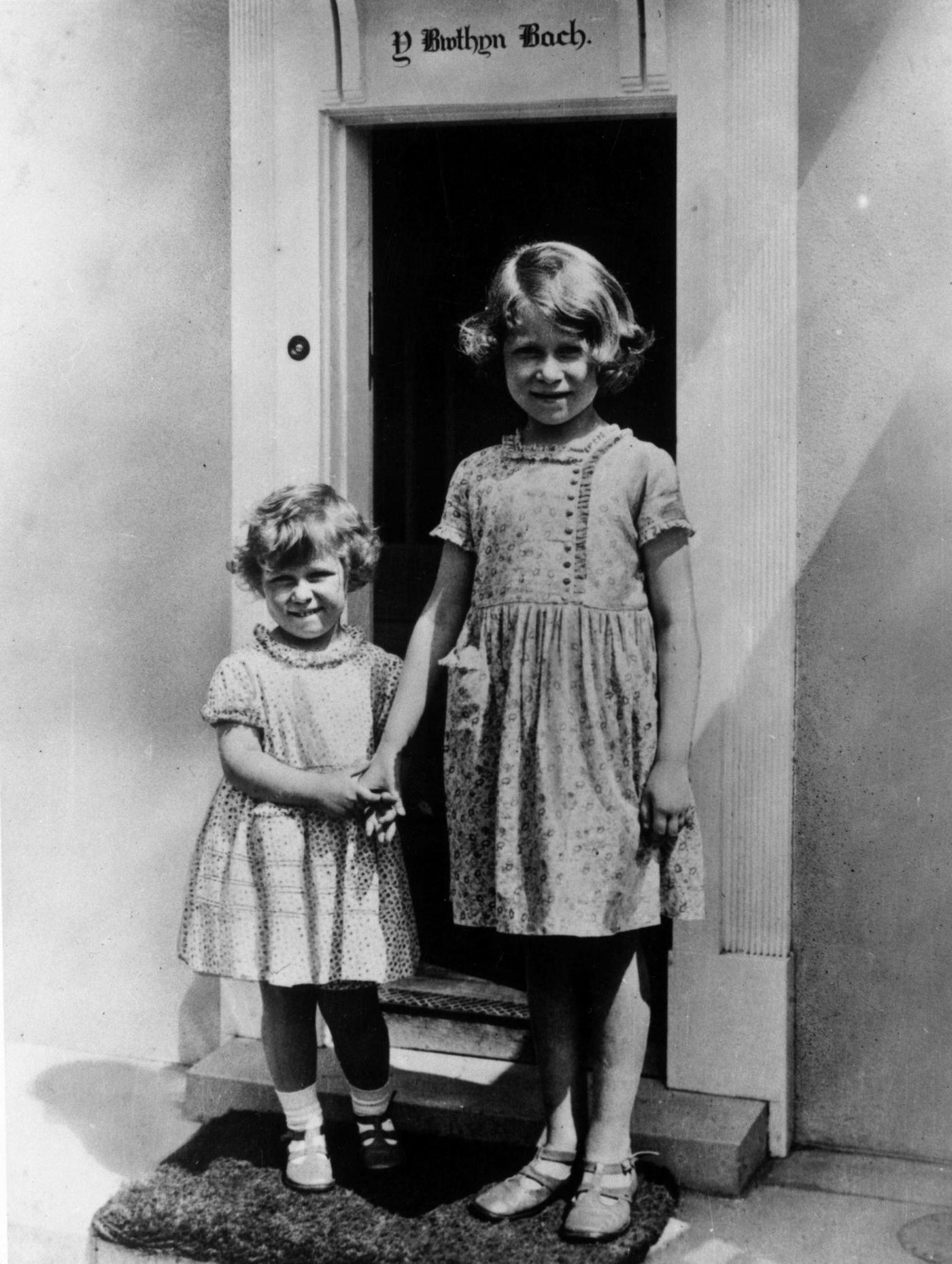 Princess Margaret Rose and Princess Elizabeth stand at the door of the Welsh House, a miniature house presented to them by the people of Wales in the grounds of the Royal Lodge, Windsor.