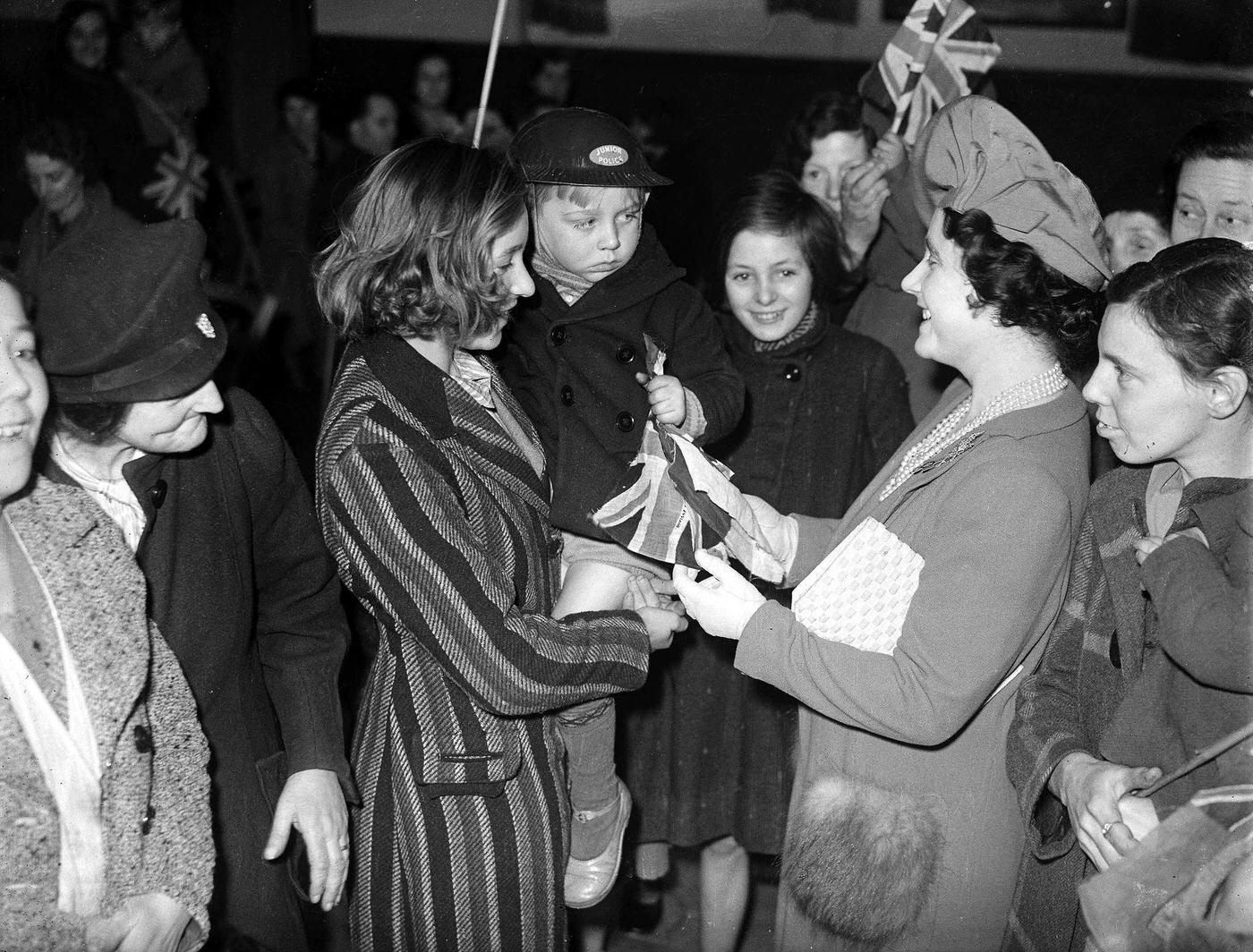 Queen Elizabeth talks to a little boy wearing a protective steel helmet during her tour of emergency feeding centres in London for people bombed out of their homes.