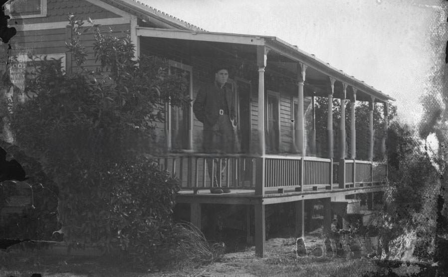 Exterior view of a man standing on the porch of a house, 1890