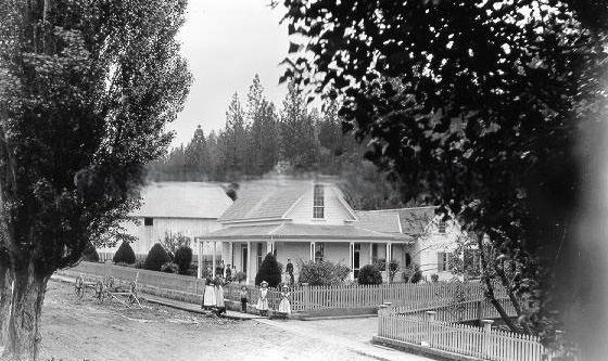Large family group stands in front of house and fence, 1895