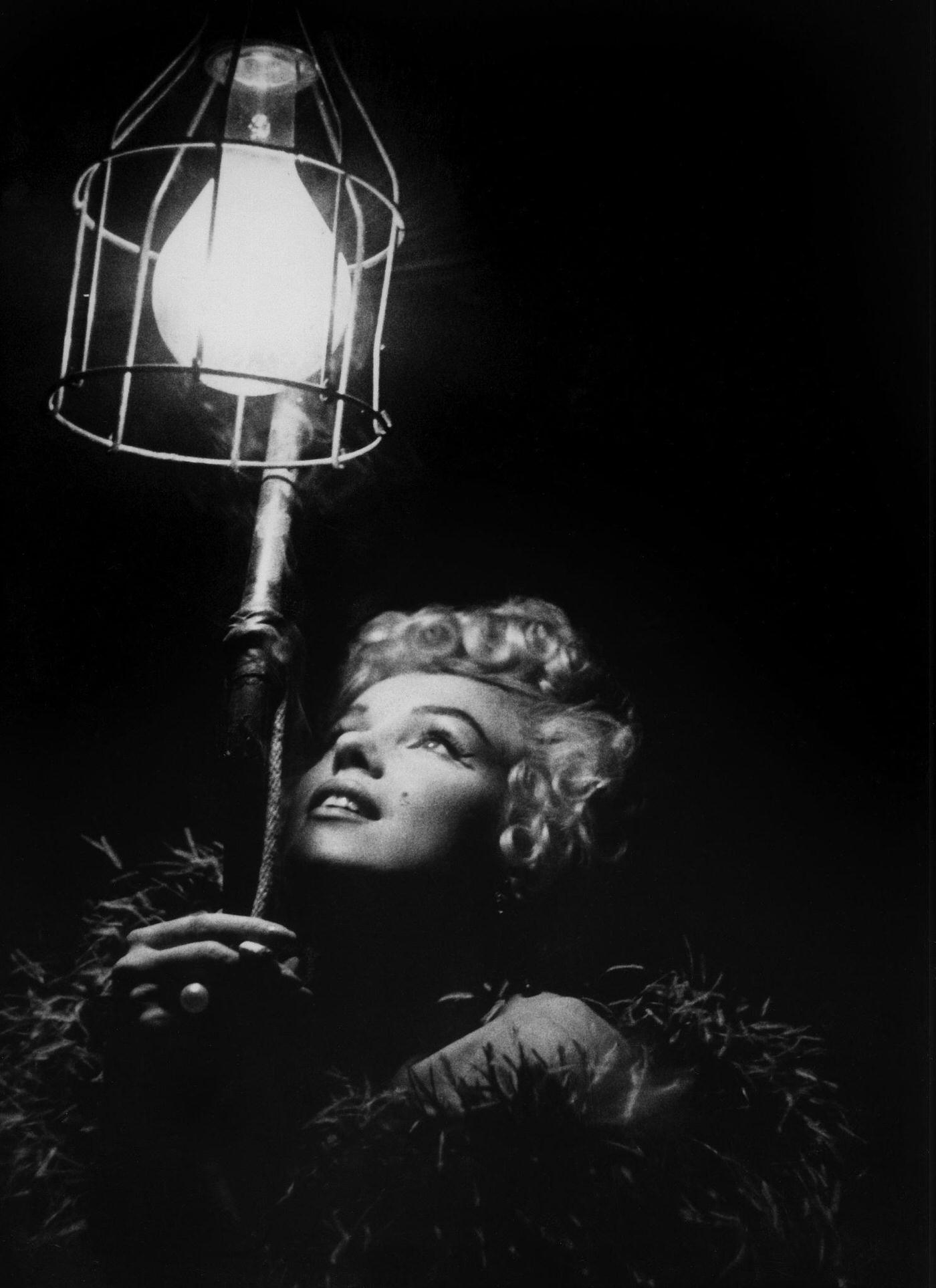 Marilyn Monroe wearing a feather boa looks up into a bright light in 1954 during the filming of "The Seven Year Itch"
