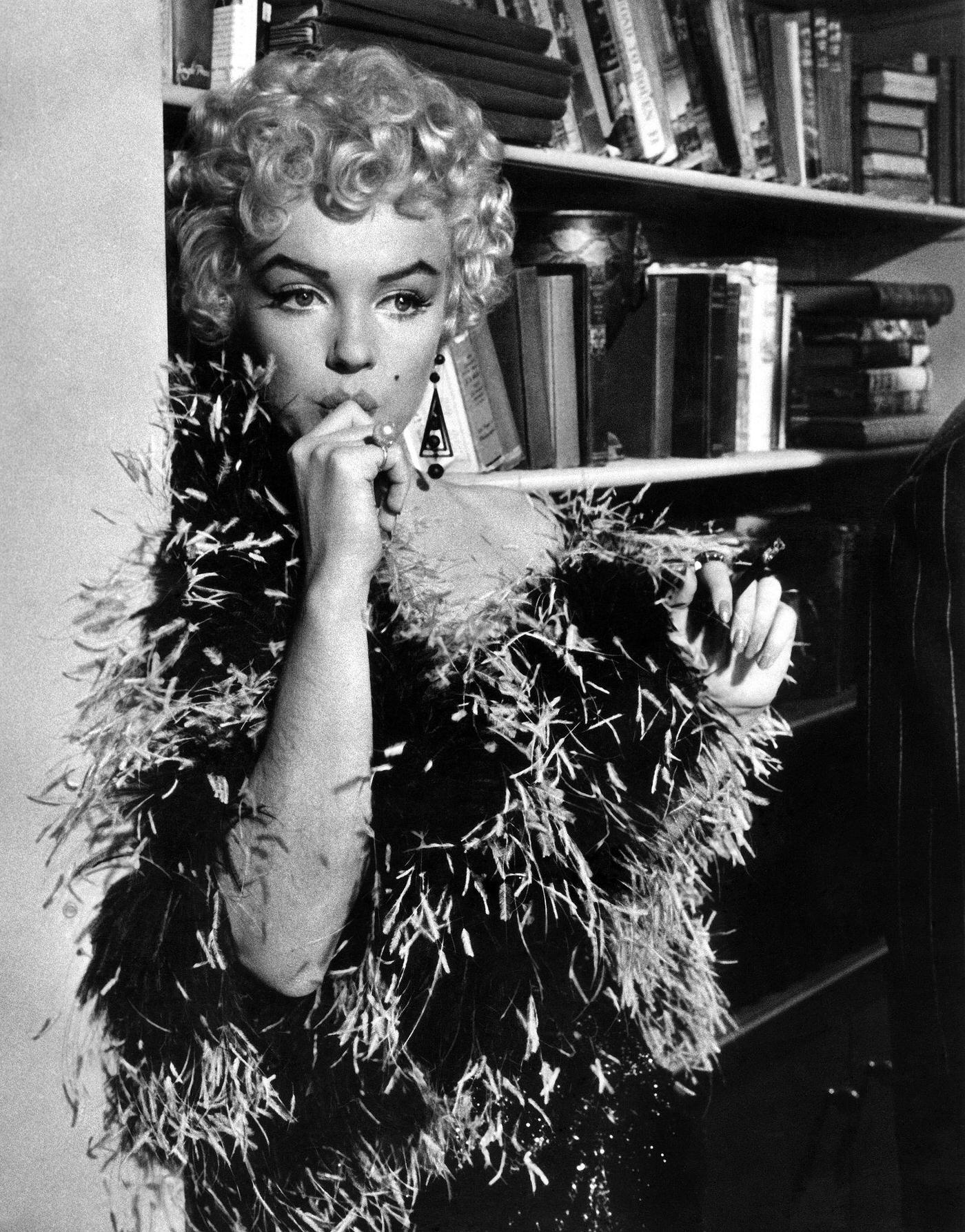 Marilyn Monroe stands in front of a bookcase wearing a feather boa in 1954 during the filming of "The Seven Year Itch"