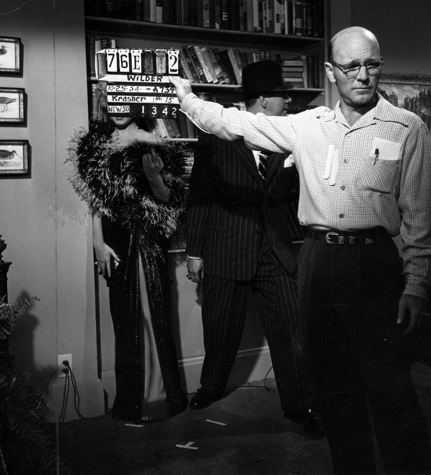 Marilyn Monroe wearing a feather boa while working on a scene with a crew-member holding a film clapper board and actor Robert Strauss