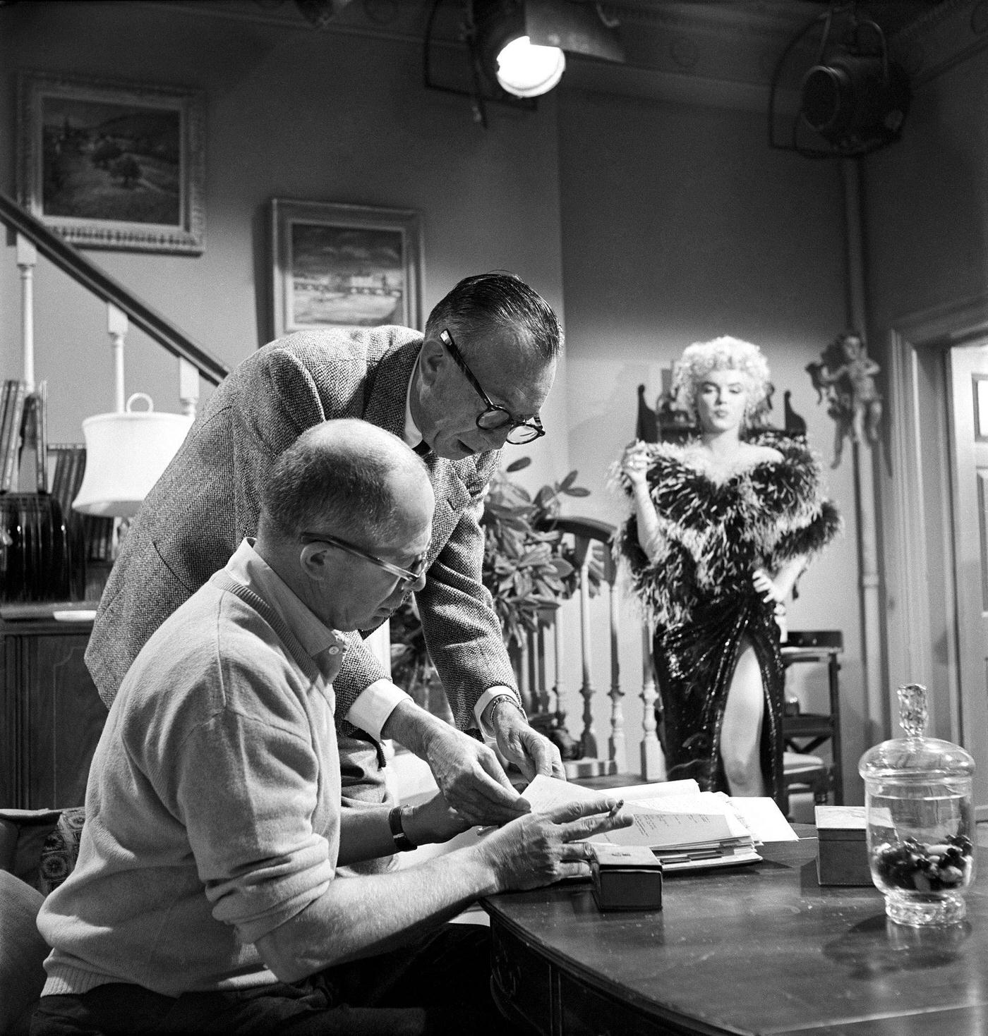 Marilyn Monroe wearing a feather boa while working on a scene with director Billy Wilder, seated at a table, 1954