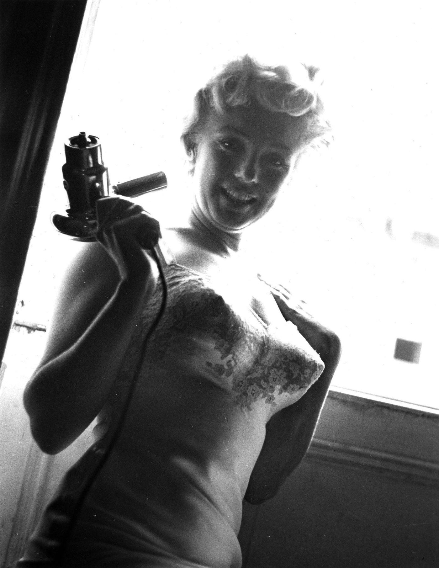 Marilyn Monroe kneels by an open window holding a hair dryer in 1954 during the filming of "The Seven Year Itch" in New York