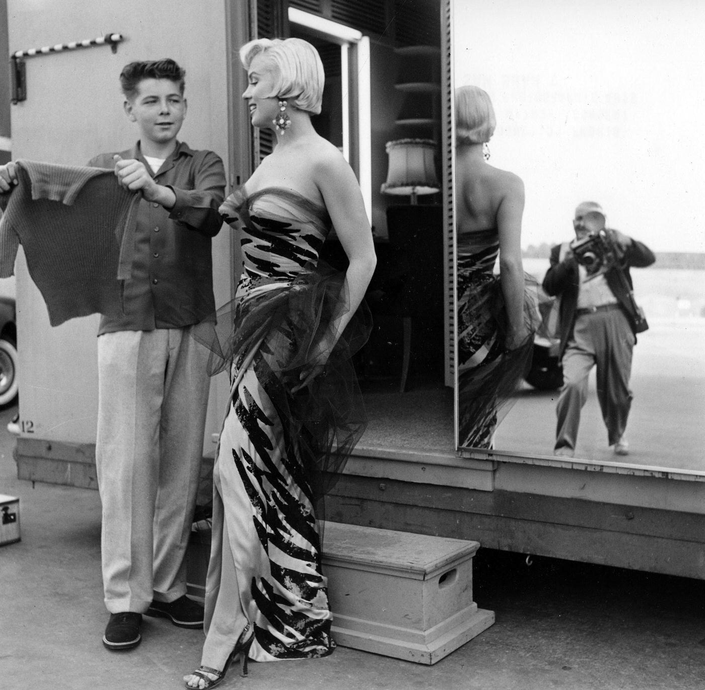 Marilyn Monroe wearing a tiger-striped dress talks to a boy on set, with the photographer Frank Powolny