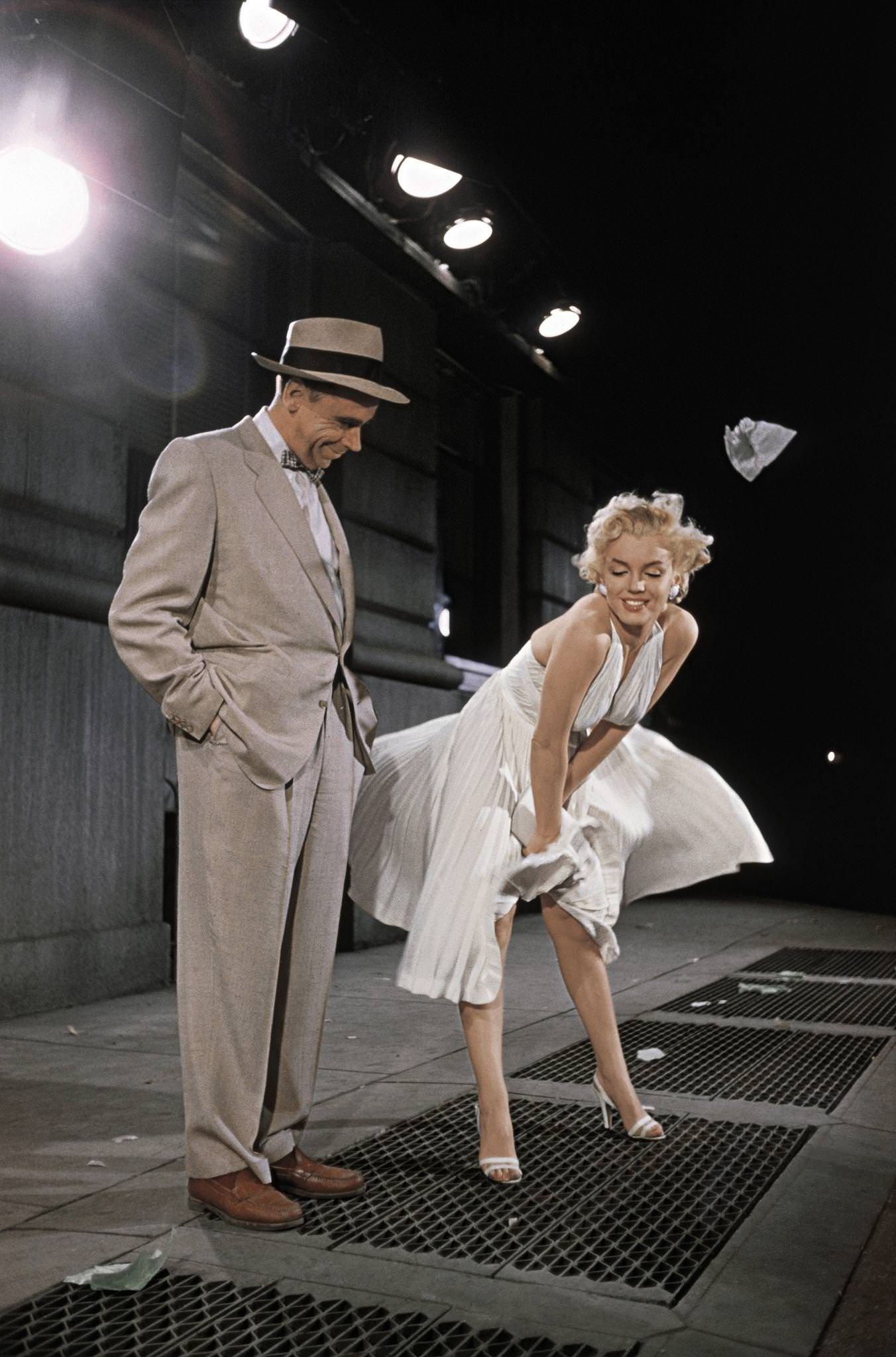 Marilyn Monroe standing over a subway grate with her white dress blowing and co-star Tom Ewell looking on in 1954 during the filming of "The Seven Year Itch"