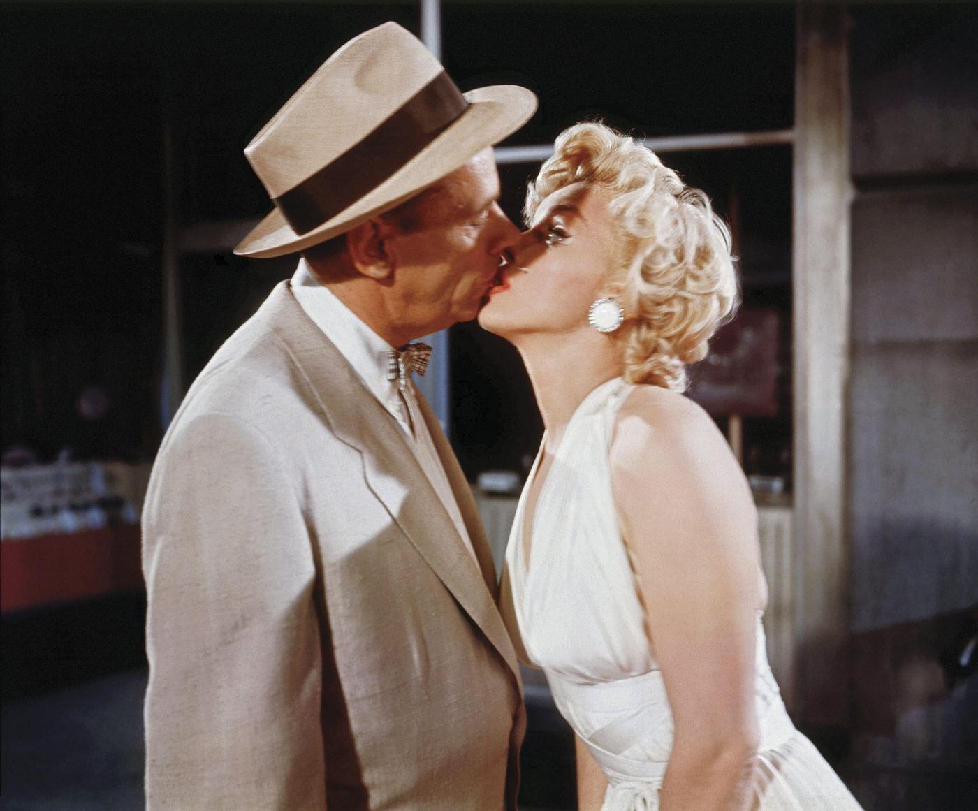 Marilyn Monroe kisses co-star Tom Ewell while wearing a white dress during the making of the famous skirt-blowing scene on set in 1954 during the filming of "The Seven Year Itch"
