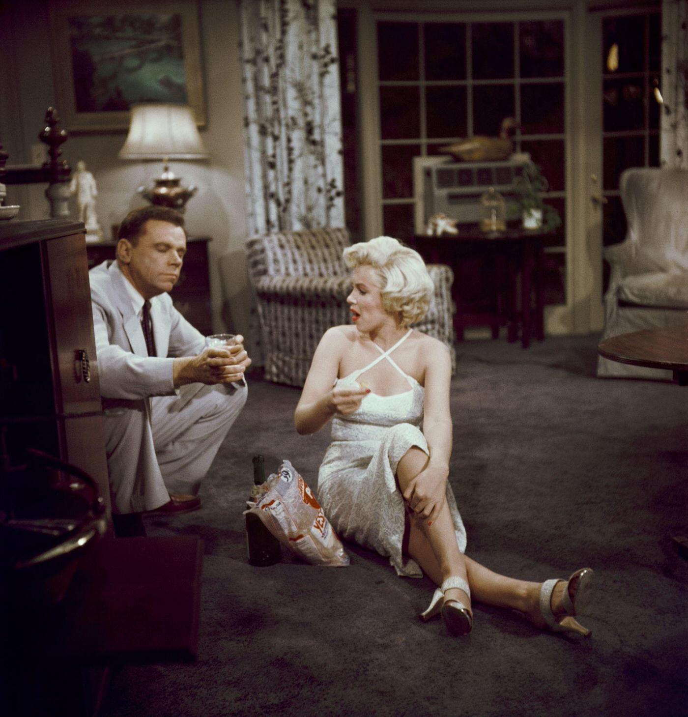 Marilyn Monroe eats potato chips and drinks champagne sitting on the floor with co-star Tom Ewell in 1954 during the filming of "The Seven Year Itch"