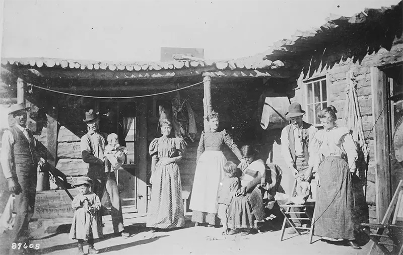 A family poses outside their home in New Mexico in 1895. Note the Native American servant holding their child.