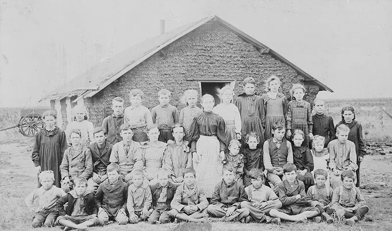 This photograph from 1895 shows a teacher and her students posing in front of a sod schoolhouse in Woods County, Oklahoma.