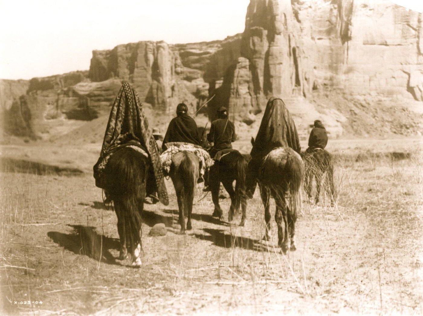 Rear view of Navajo Indians on horseback making their way over the sparse, dry, grassy floor of Tesacod Canyon, 1905