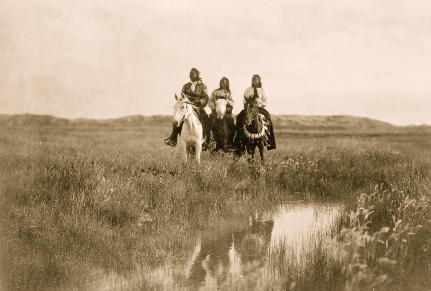 Three Sioux Indians on horseback facing front by pond on plains, 1905