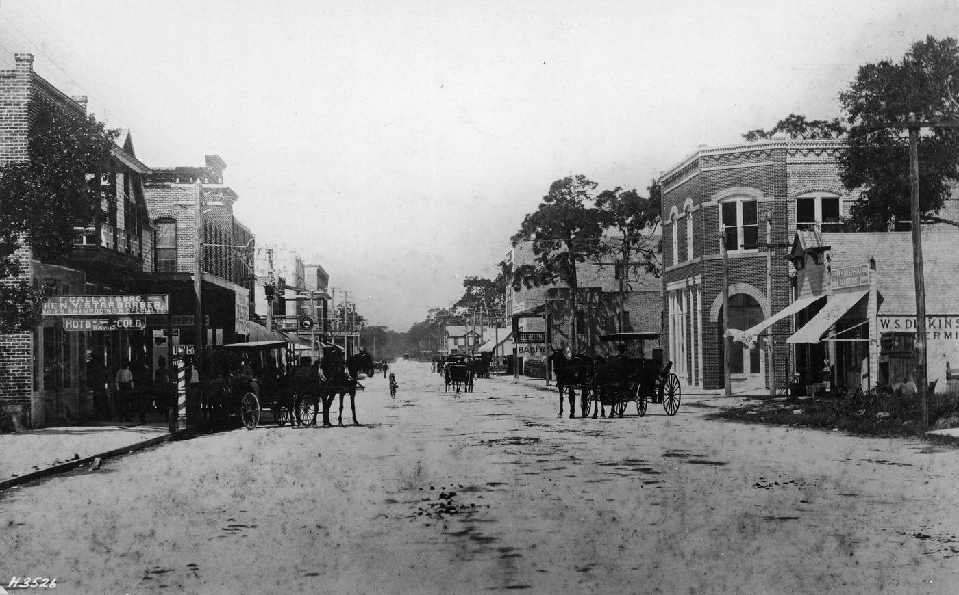 Horses, carriages, and pedestrians are seen as one looks West along the shops which line unpaved Flagler Street, Miami, Florida, circa 1900.