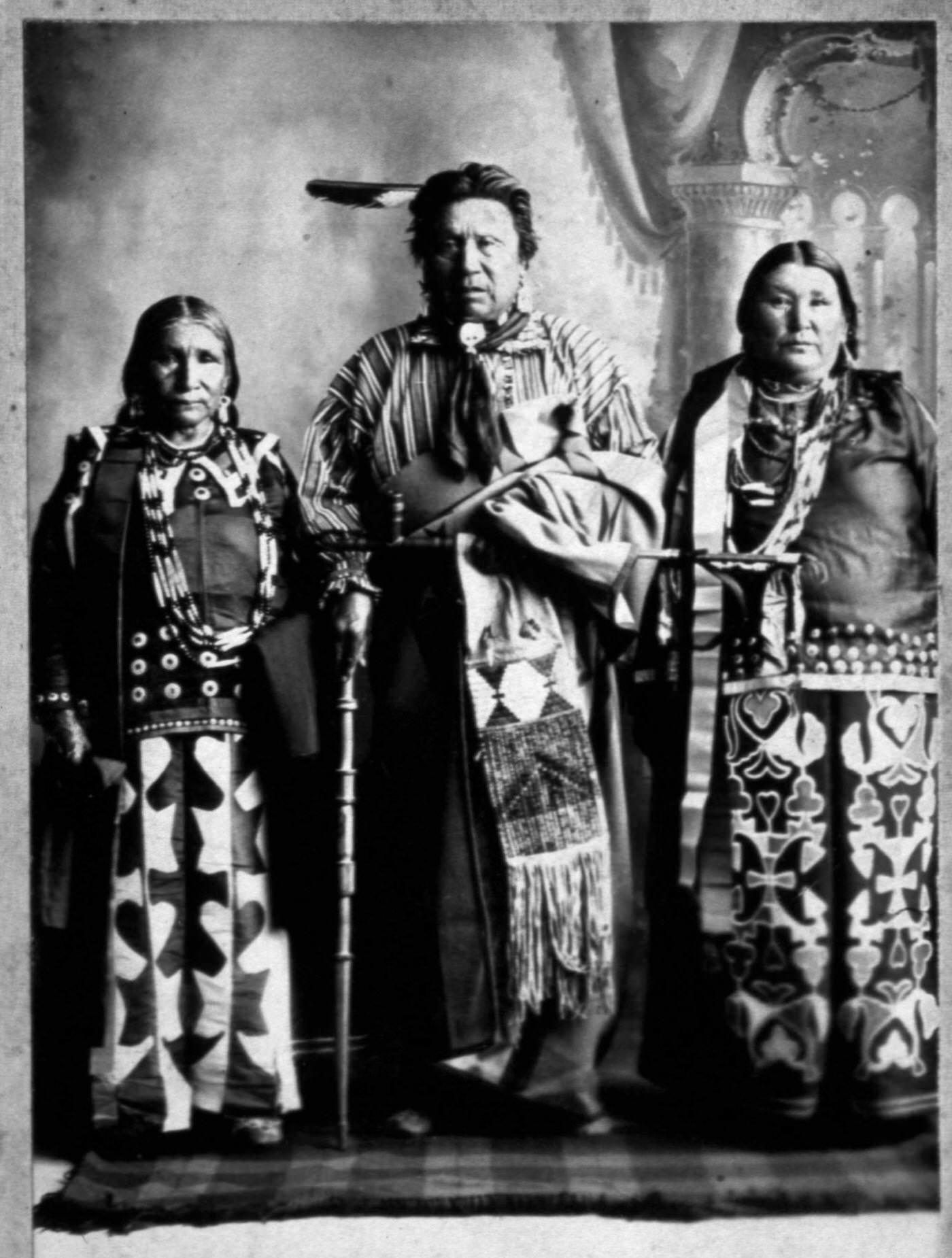 Three Iowa Native Americans pose in a studio with all their finest accouterments for a photo.